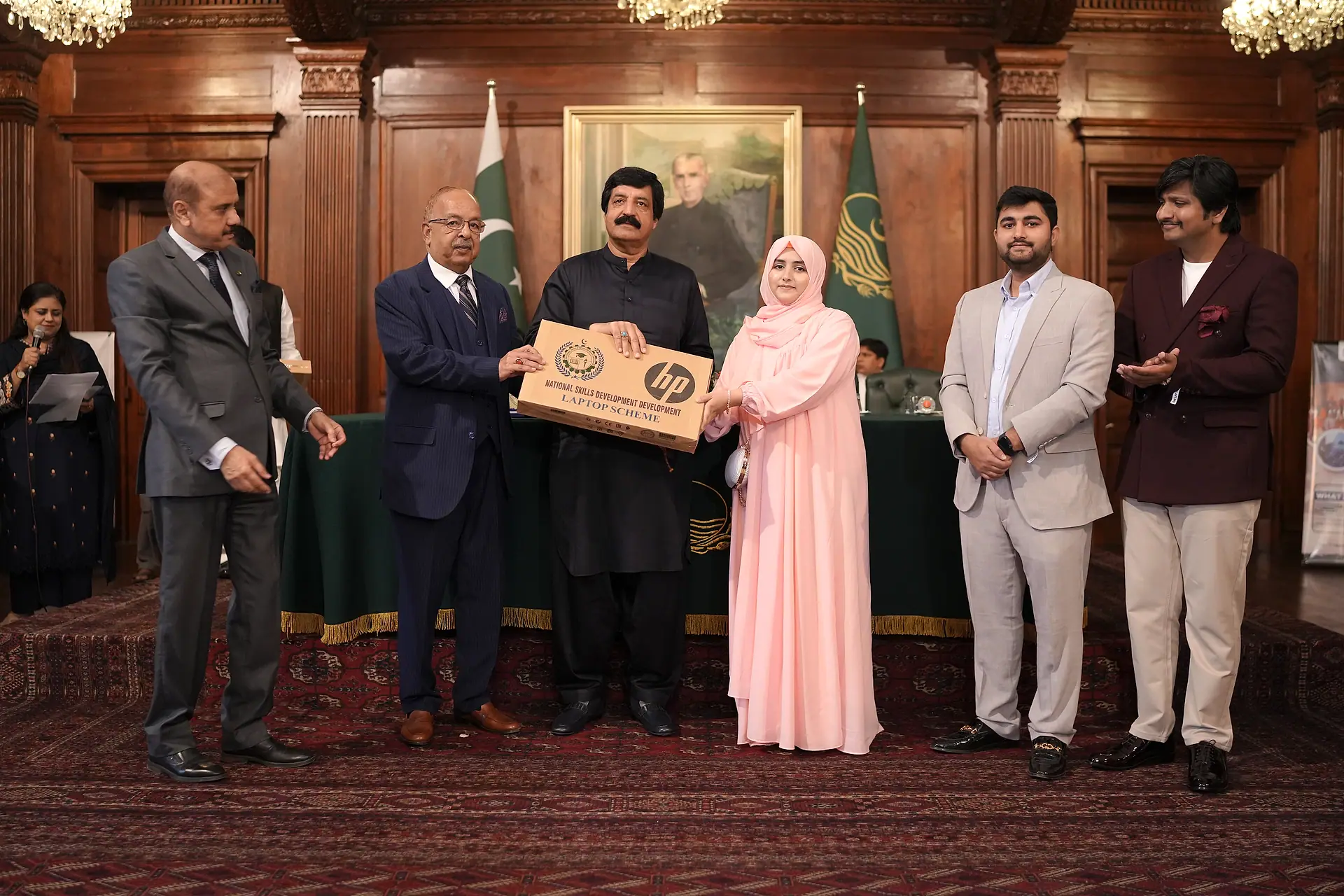 The Governor of Punjab and a student hold her laptop box on stage